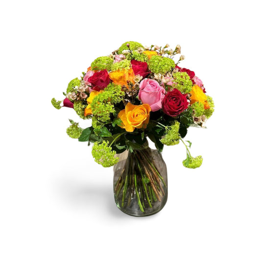 Der Blumenstrauß „Golden Sunrise“ von florali besteht aus einer klaren Glasvase, gefüllt mit roten, rosa und gelben Rosen, akzentuiert mit Eukalyptus, grünem Laub und kleinen weißen Blüten – alles vor einem weißen Hintergrund.