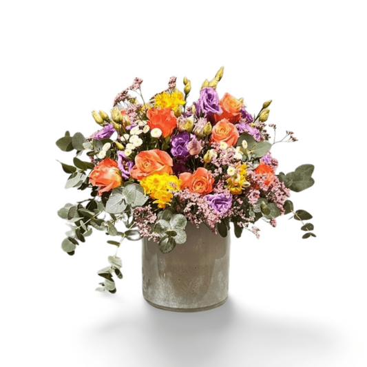 Der florali Muntermacher verfügt über eine Metallvase mit einer lebendigen Mischung aus orangefarbenen Rosen, lila Lisianthus, gelben Blüten, weißen Knospen, rosa Füllblumen und grünen Eukalyptus, kunstvoll arrangiert vor weißem Hintergrund.