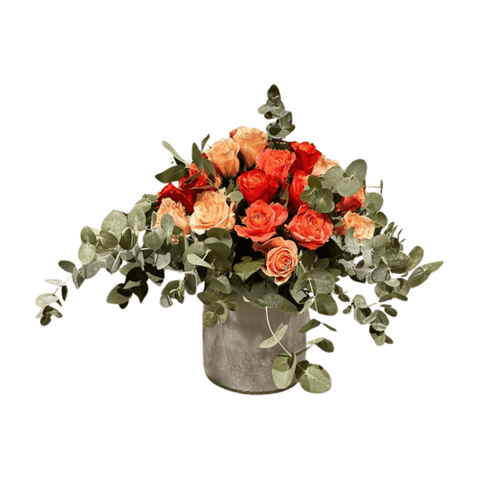 Der Blumenstrauß „Little K“ von florali besteht aus orangefarbenen und pfirsichfarbenen Rosen mit Eukalyptus in einer grauen zylindrischen Vase, isoliert auf weißem Hintergrund.