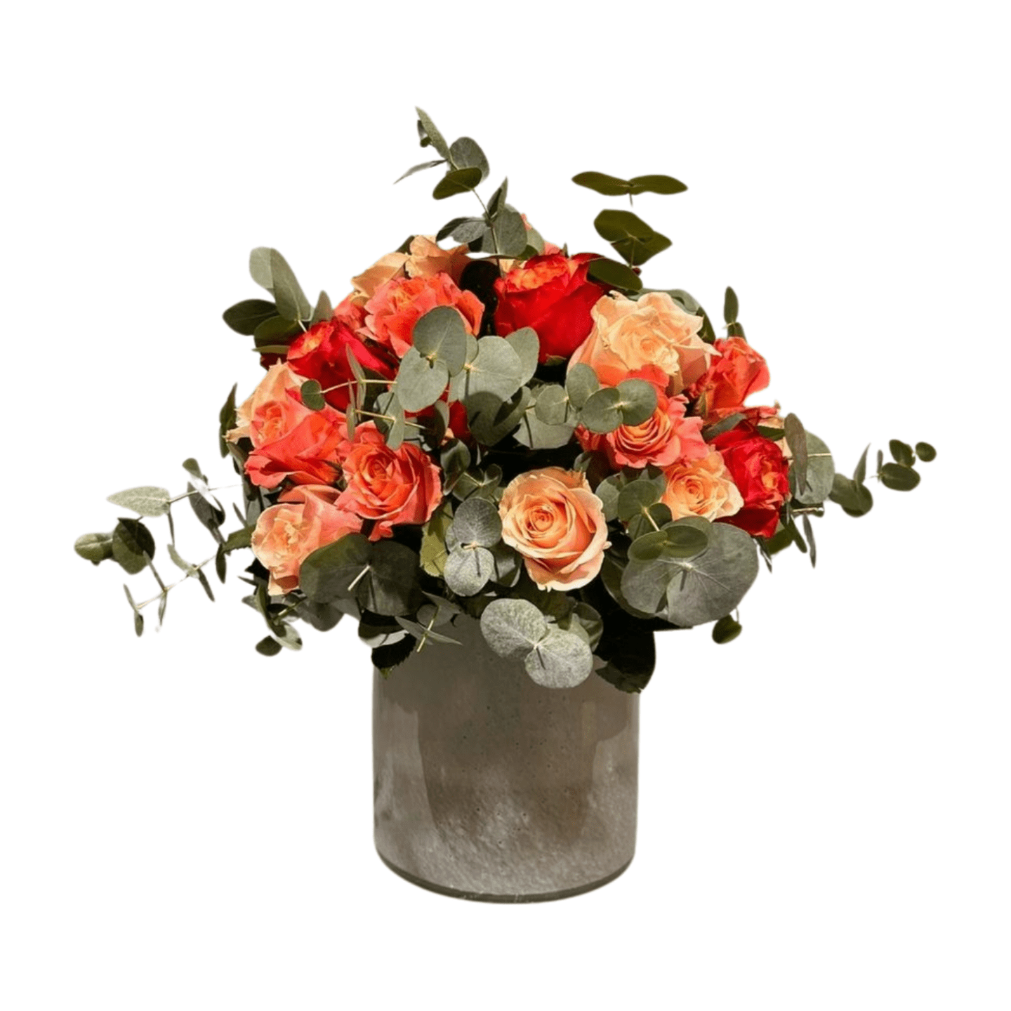Das Florali Little K besteht aus orangefarbenen und pfirsichfarbenen Rosen mit grünen Eukalyptusblättern, arrangiert in einer runden grauen Vase vor einem weißen Hintergrund.